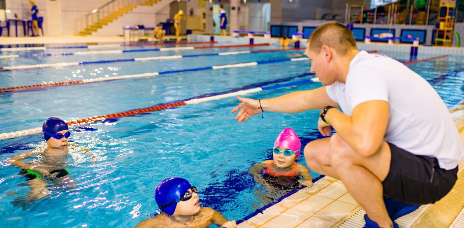 Disabled boy with Down syndrome in swimming cap wearing goggles in swimming pool